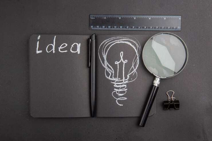 Top view of tools for creative writing – notebook, binder clip, magnifying glass, ruler, and pen.