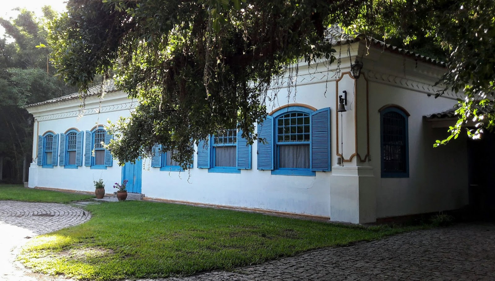 Grande casa em estilo colonial, com seis janelas e uma porta centralizada pintadas de azul claro, em destaque com o branco das paredes.