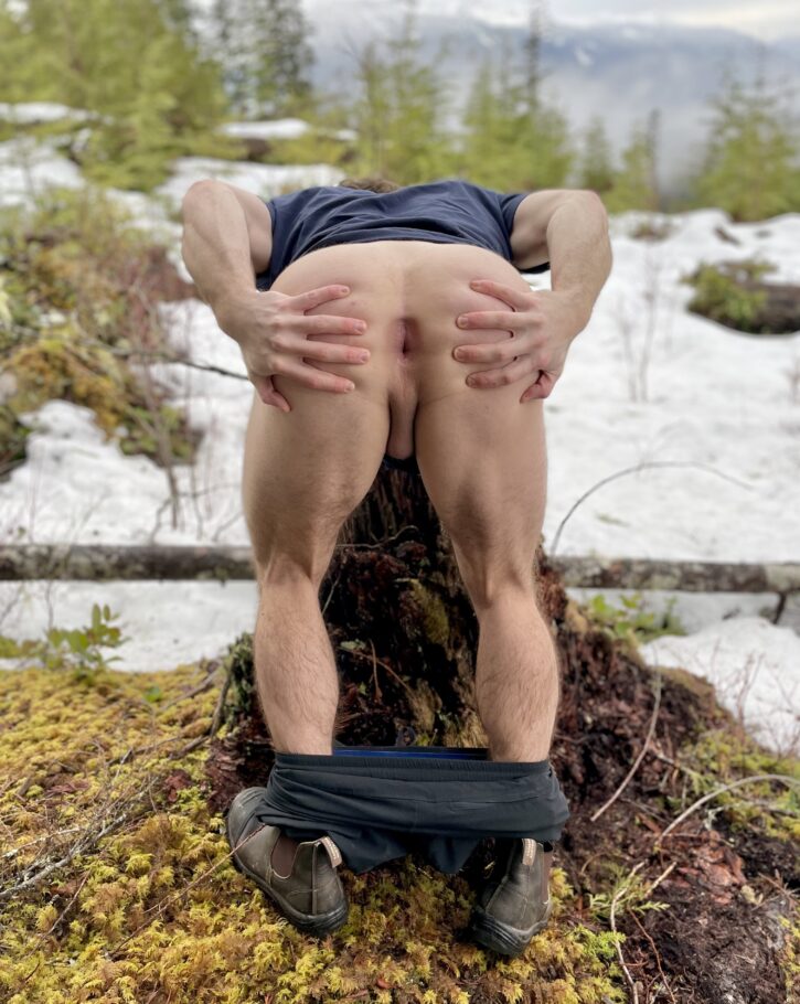 Hole Next Door with his pants around his ankles in the woods leaning forward to show off his stretched hairless asshole ready for cock