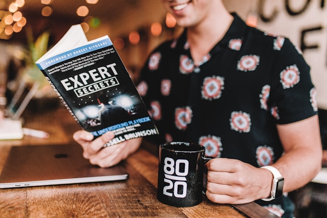 A man reading a book titled "Expert Secrets" while drinking coffee