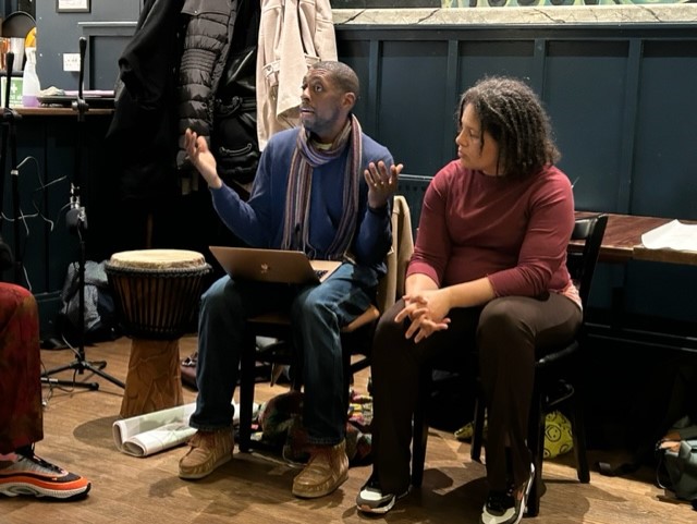 Phillip Beckles-Raymond and Gabriella Beckles-Raymond presenting their work to the group, sitting next to Phillip's drum.