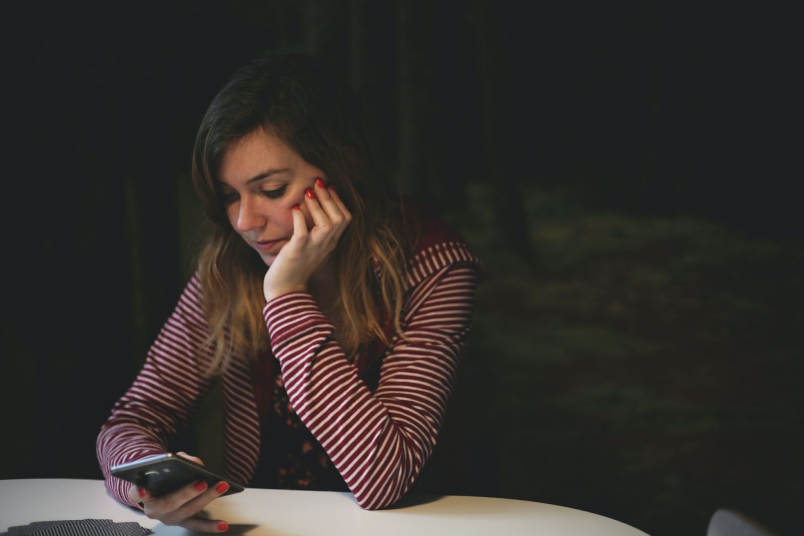 Woman leaning on white table holding her smartphone looking disappointed.