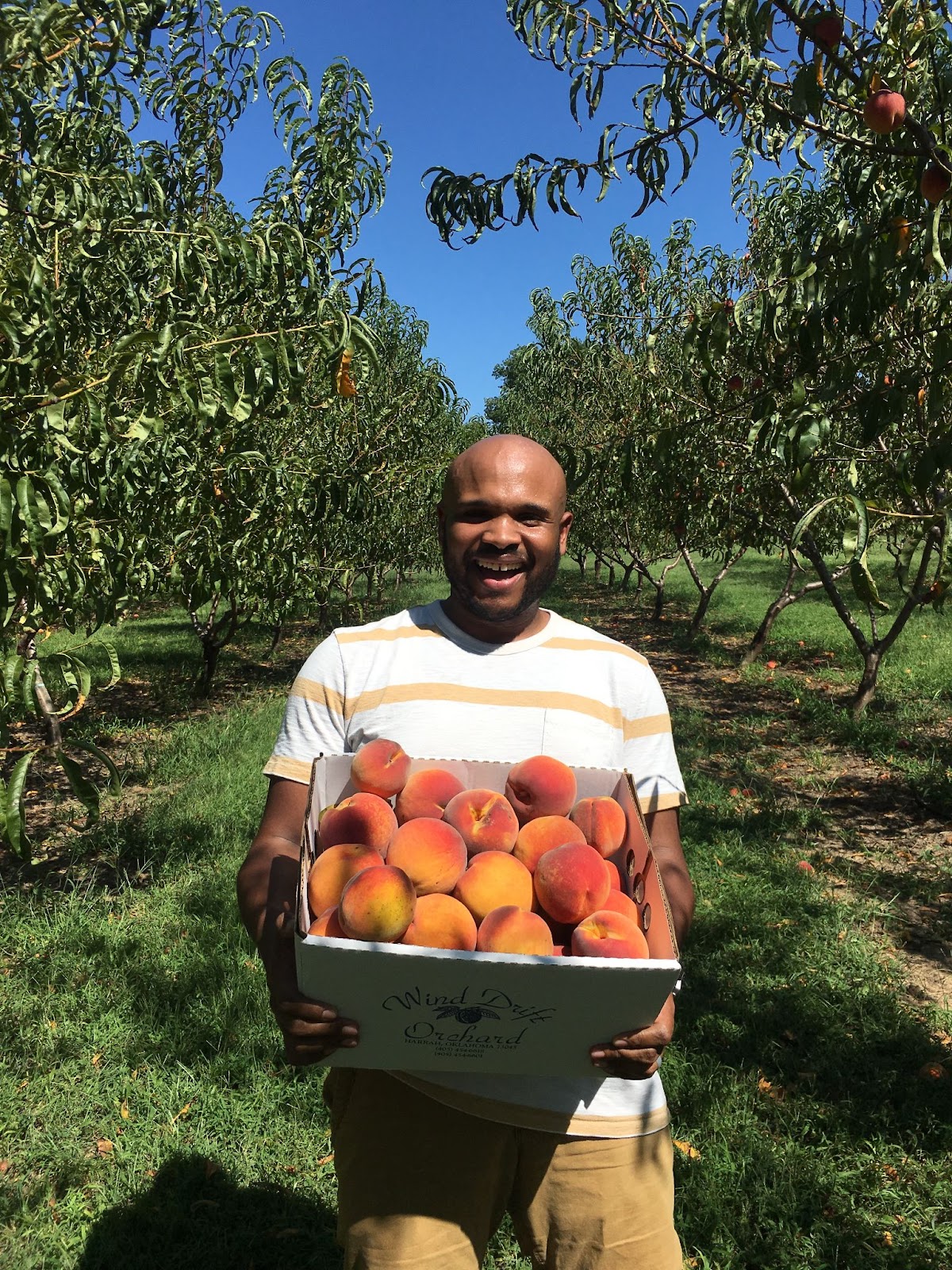 John posing for a photo while holding a box full of ripe peaches.
