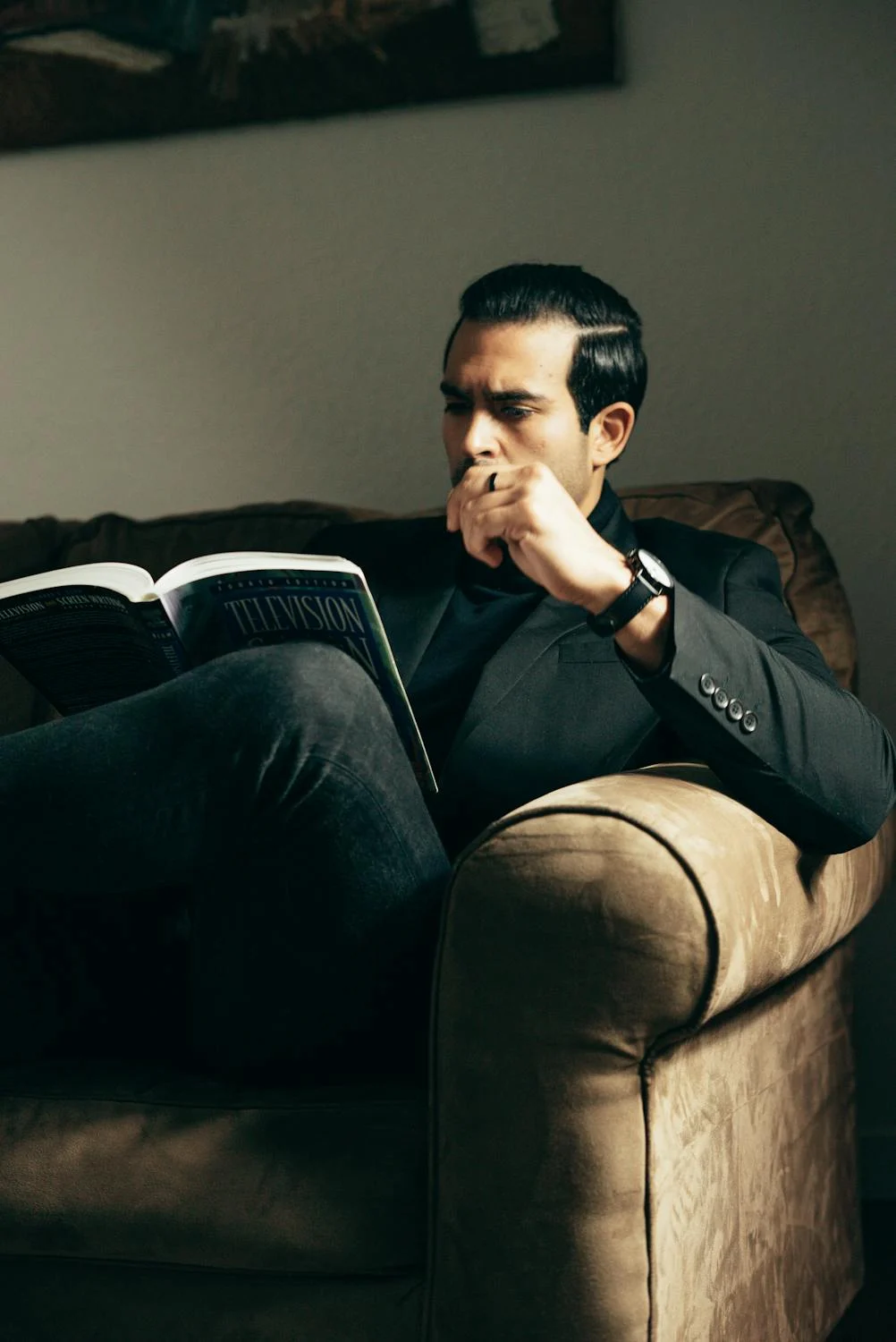 A man sitting on a sofa and reading with a book