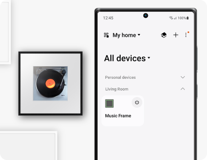 A Samsung Galaxy phone displaying the SmartThings app is positioned next to a Samsung Music Frame.