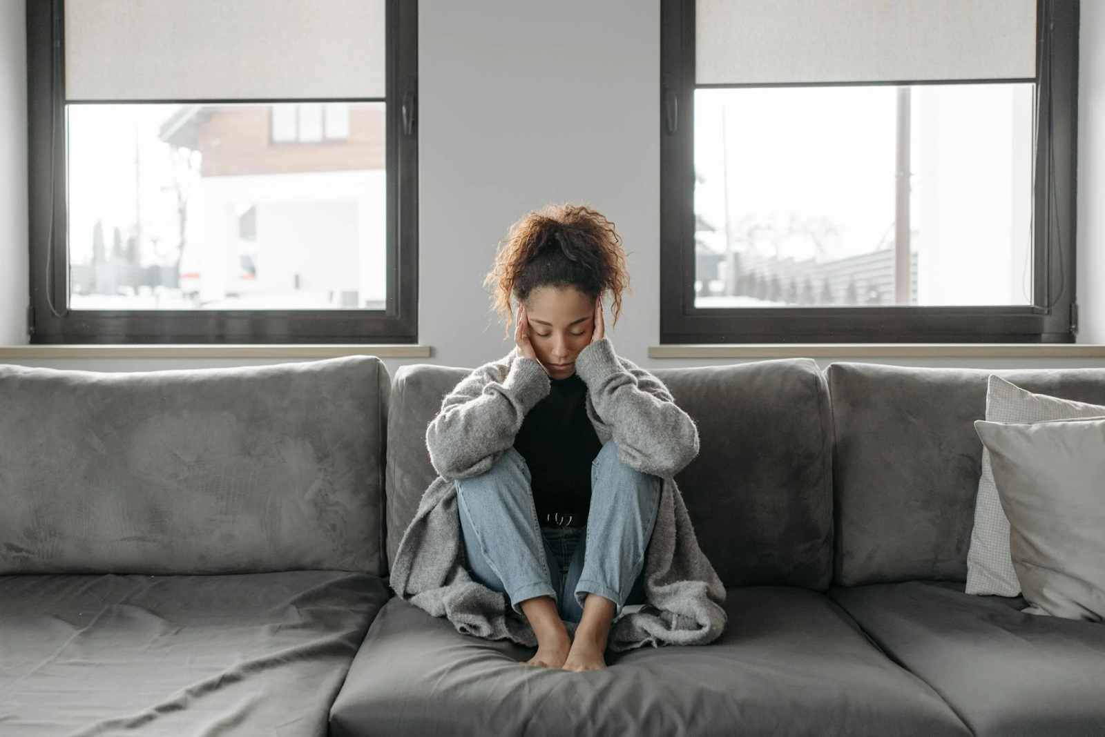 A woman sits on a couch holding her head