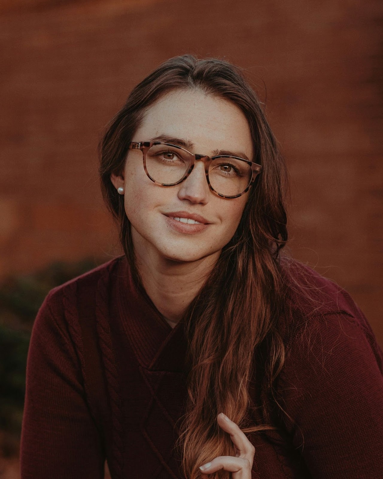 A woman is smiling while gently gliding her hand through her hair to give a warm and easygoing look for a modelling headshot