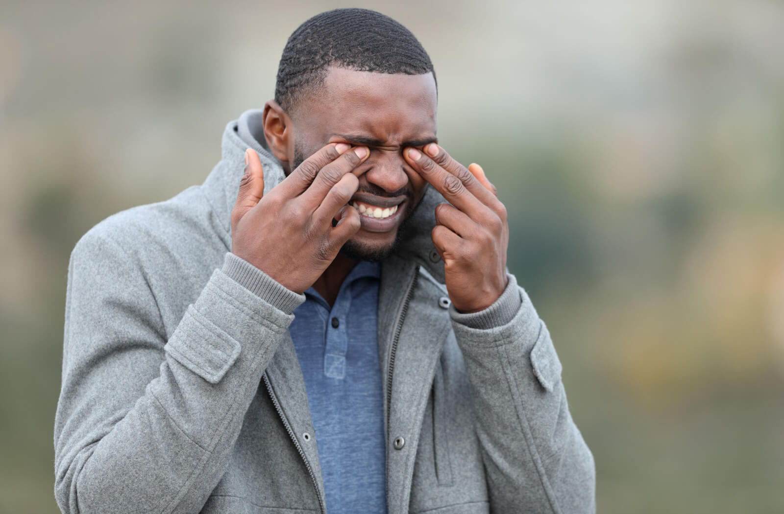A man in his jacket rubbing his eyes with both hands.