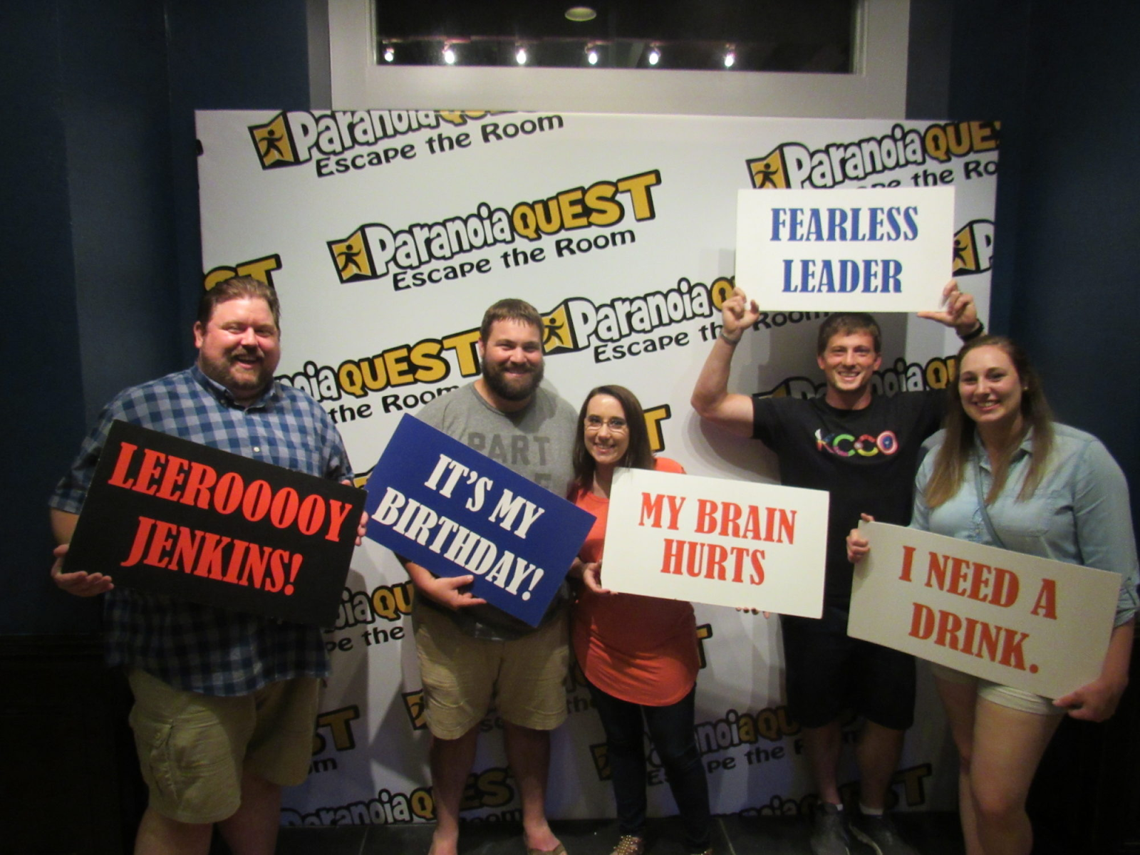 A group of friends posing with banners, celebrating their victory after winning an escape game at Paranoia Quest.