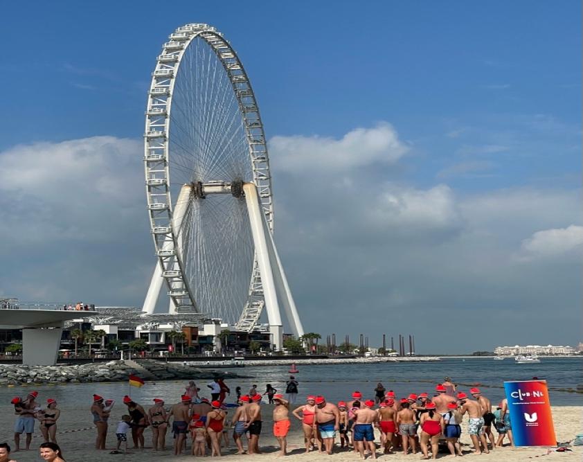 A group of people on a beach with London Eye in the background Description automatically generated