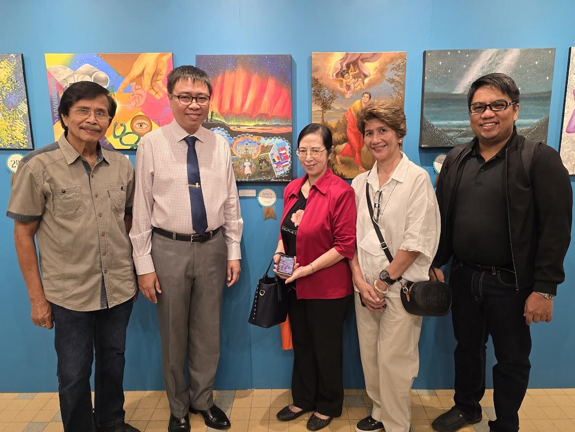 A group of people standing in front of a blue wall with paintings

Description automatically generated