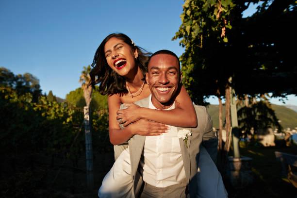 happy groom piggybacking bride in vineyard - black man love stock pictures, royalty-free photos & images