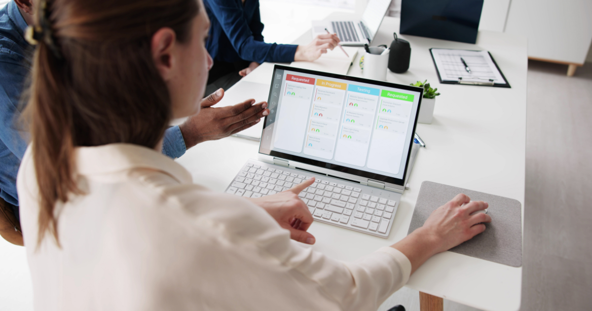 Professionals using agile project management software on a laptop during a meeting.