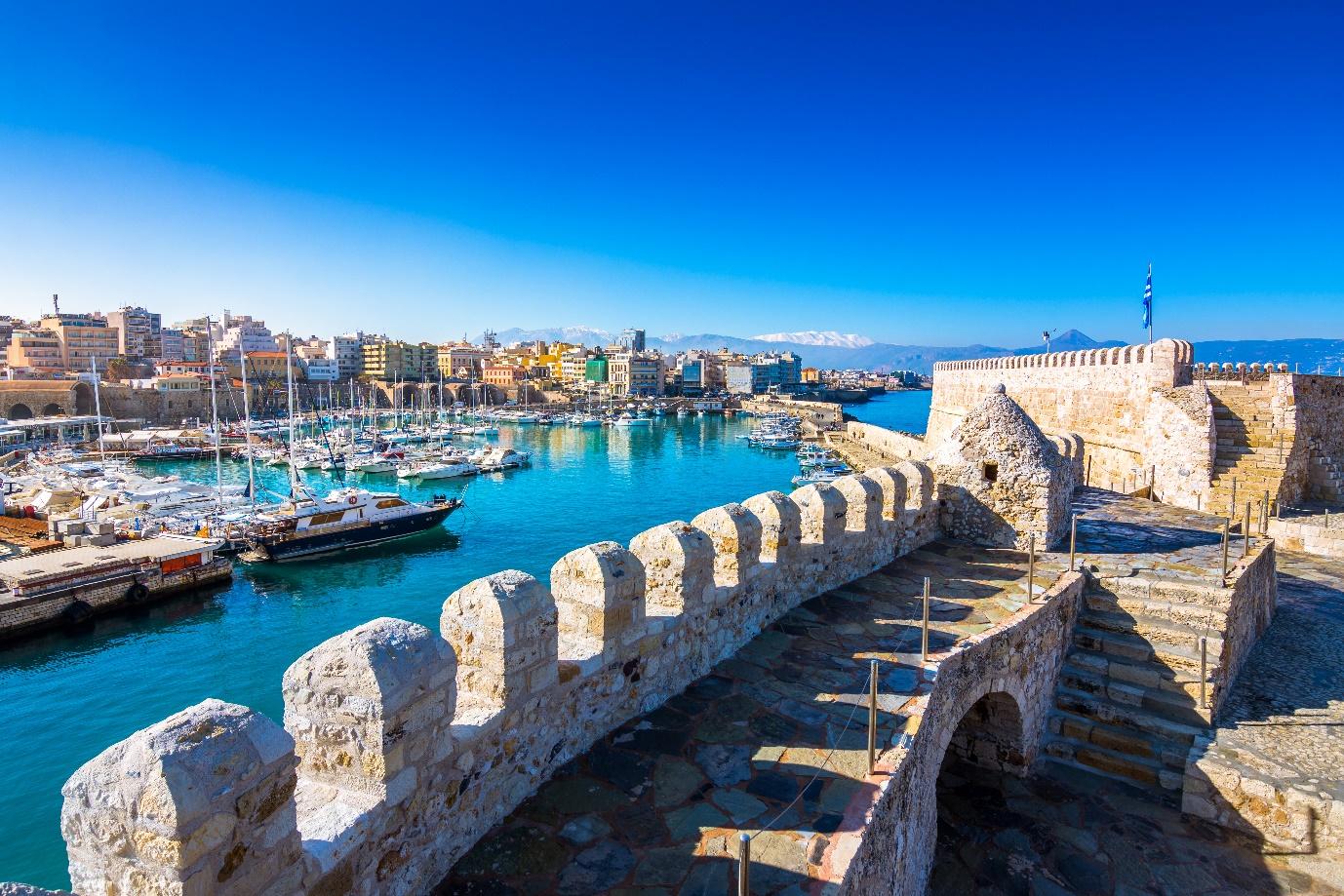 A stone wall with a body of water and boats in the background

Description automatically generated