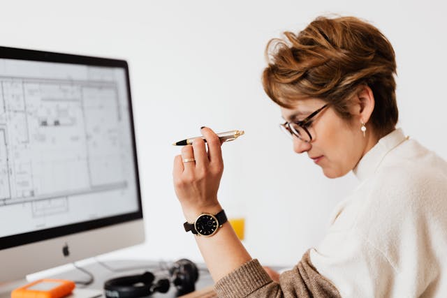 A woman typing on a computer with a pen in hand.