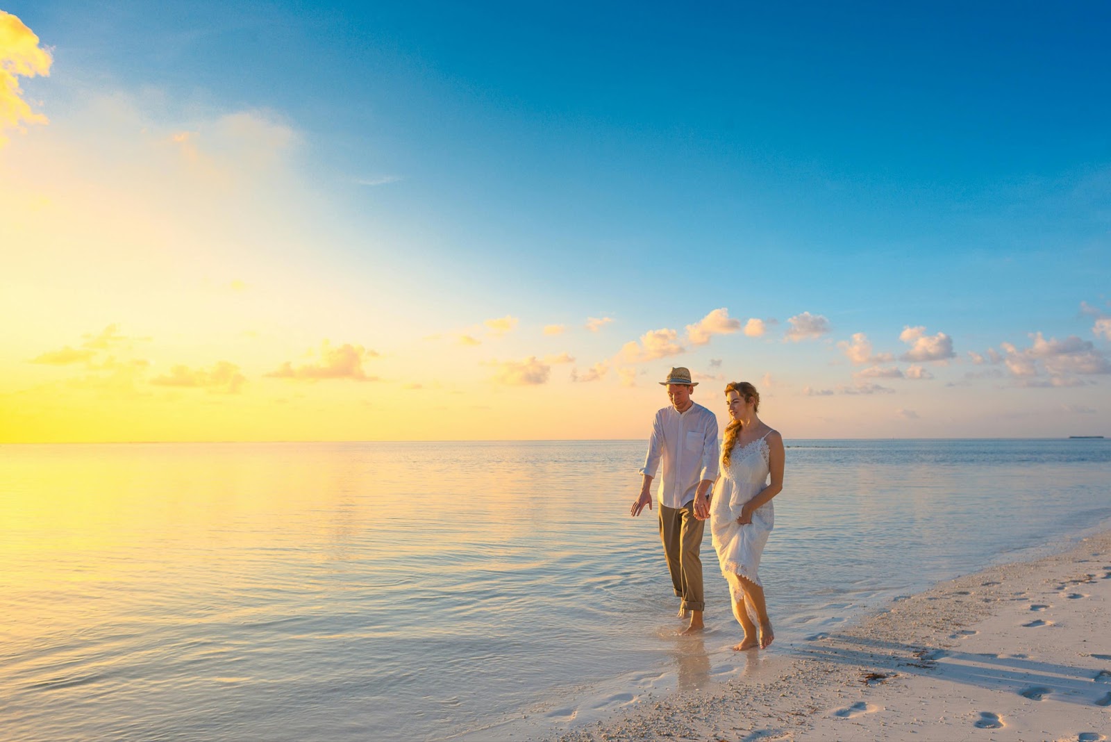 A couple walking hand in hand along a pristine beach with turquoise waters and clear blue skies.