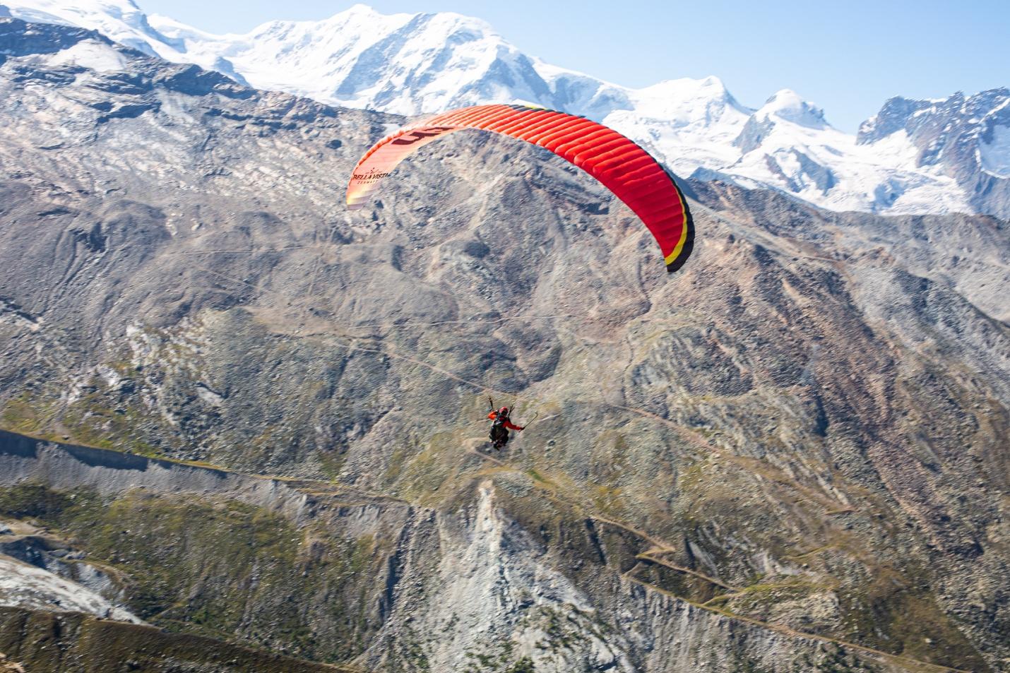 A person flying a parachute over a mountain

Description automatically generated