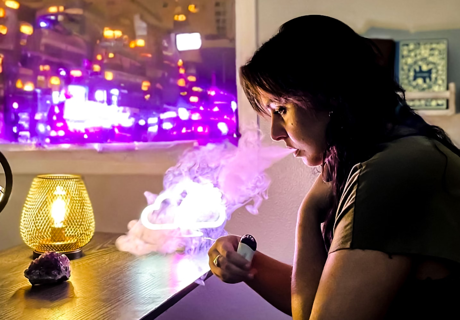 A woman sitting next to a table with light while vaping cannabis 