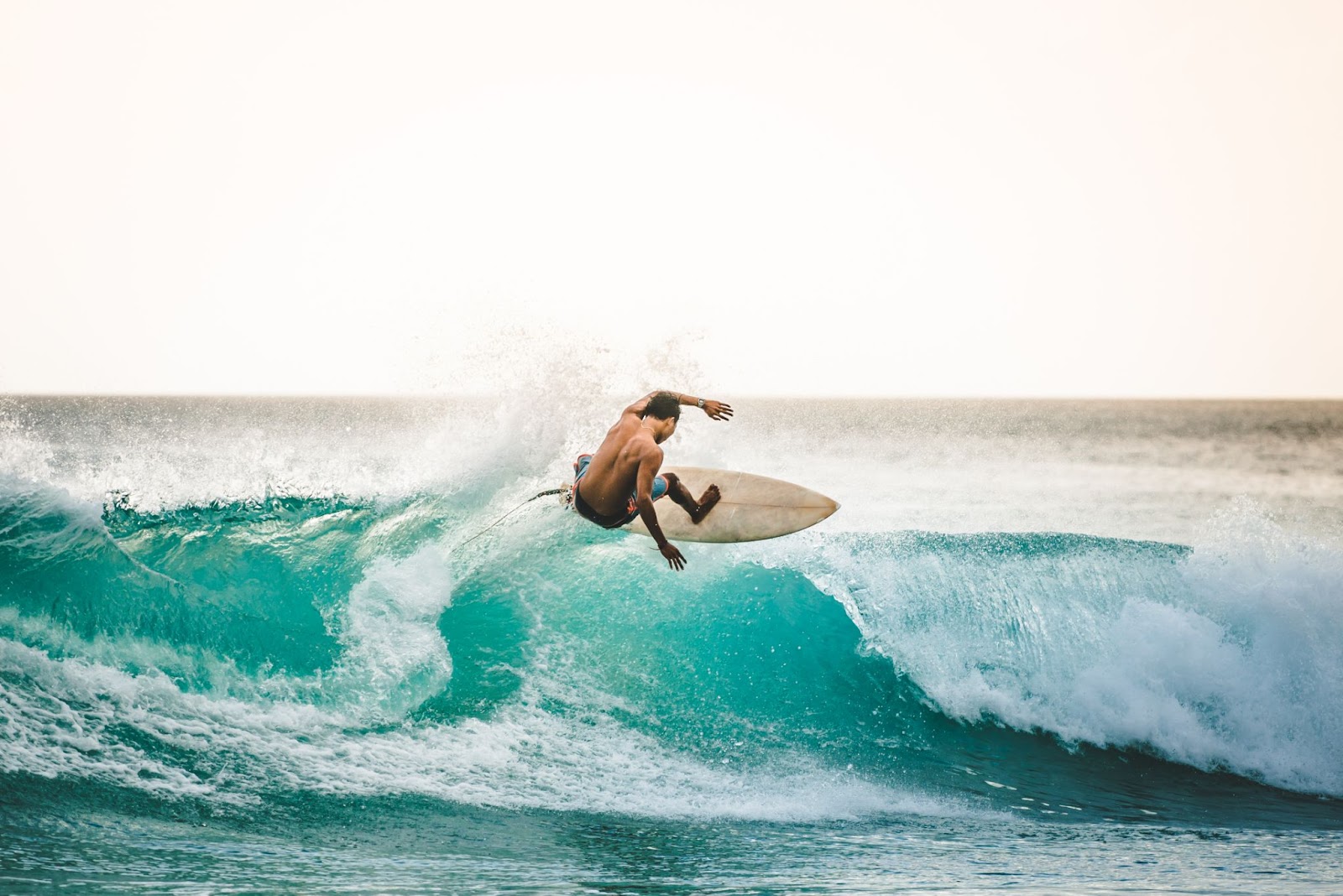 Surfista fazendo manobra com a prancha no meio de uma onda do mar.