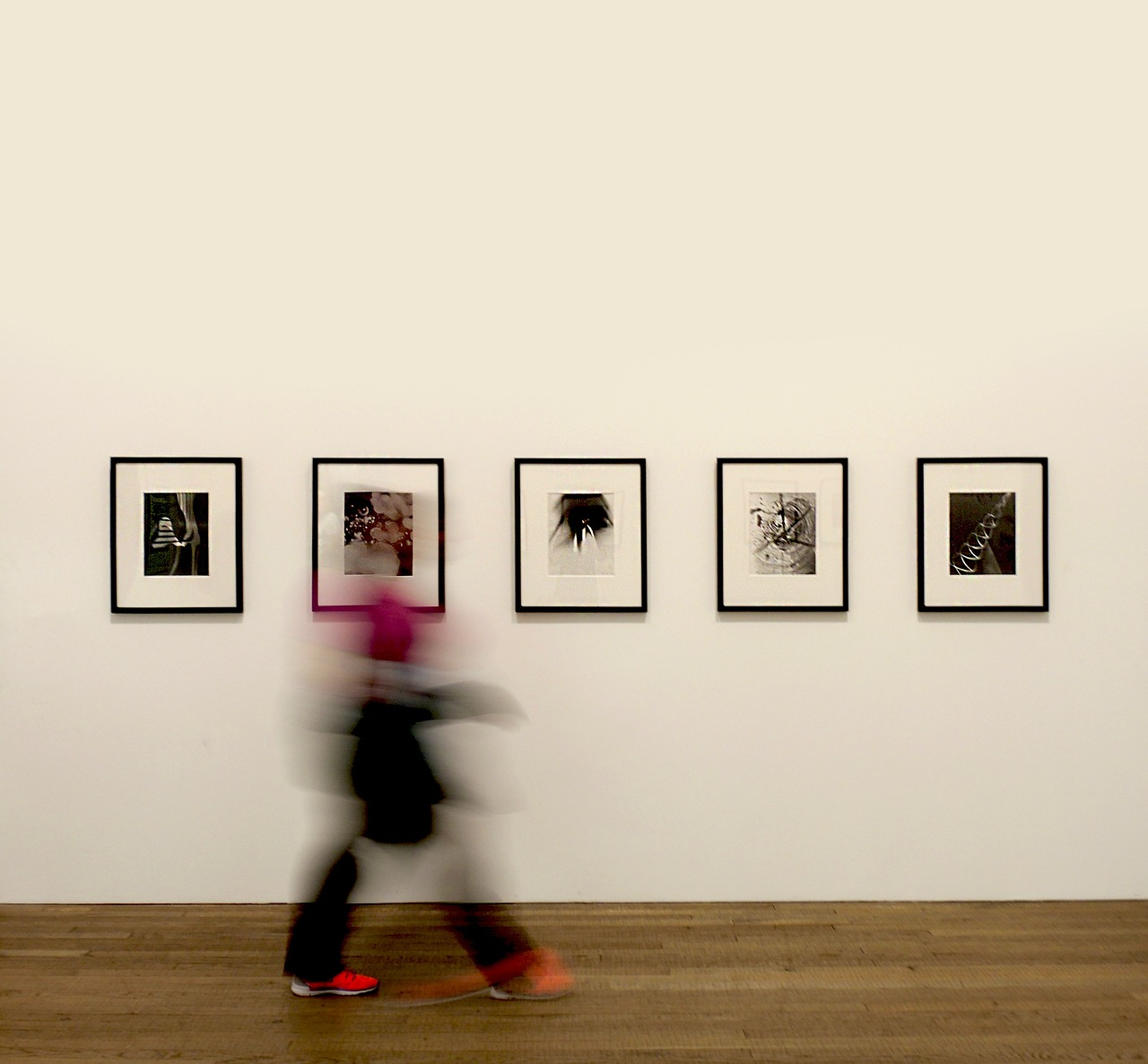 a person walking with motion blur past a series of black and white prints on a white wall