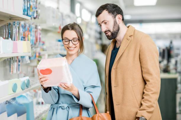 Couple in the pharmacy store Young couple choosing diapers for baby standing in the pharmacy store adult diaper stock pictures, royalty-free photos & images