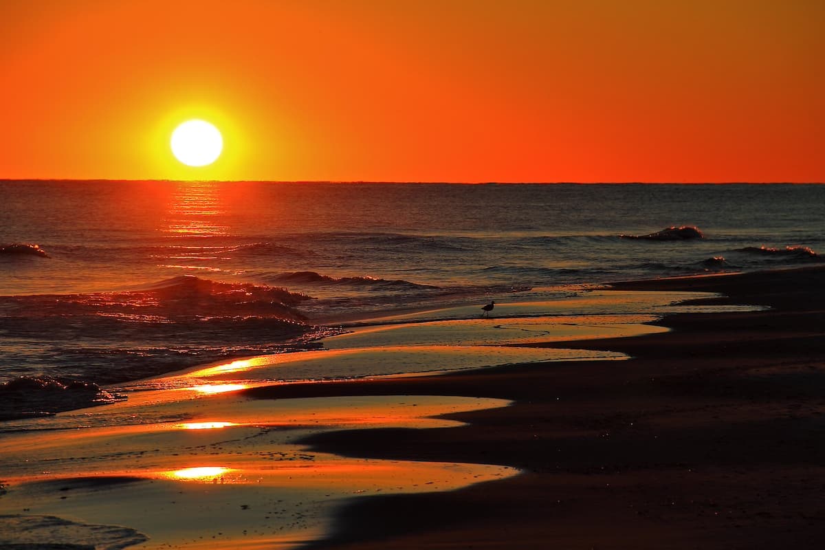 Orange sunset on Gulf Shores Beach with large yellow sun close to the horizon in background 