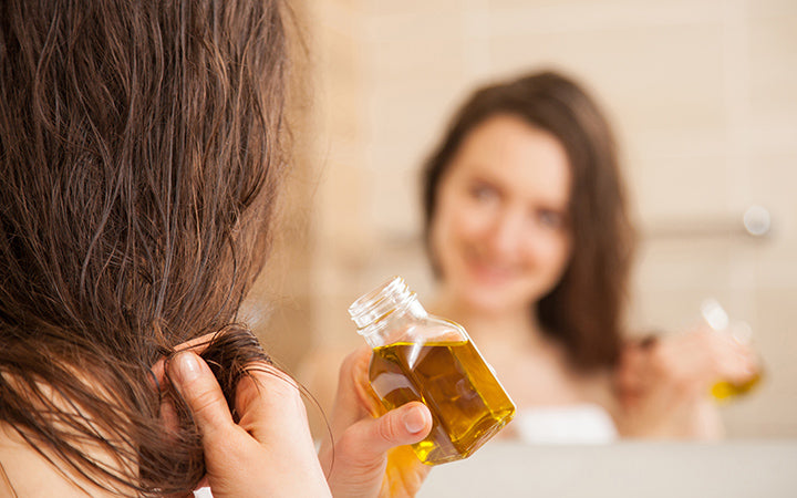 woman applying oil mask to hair tips in front of a mirror