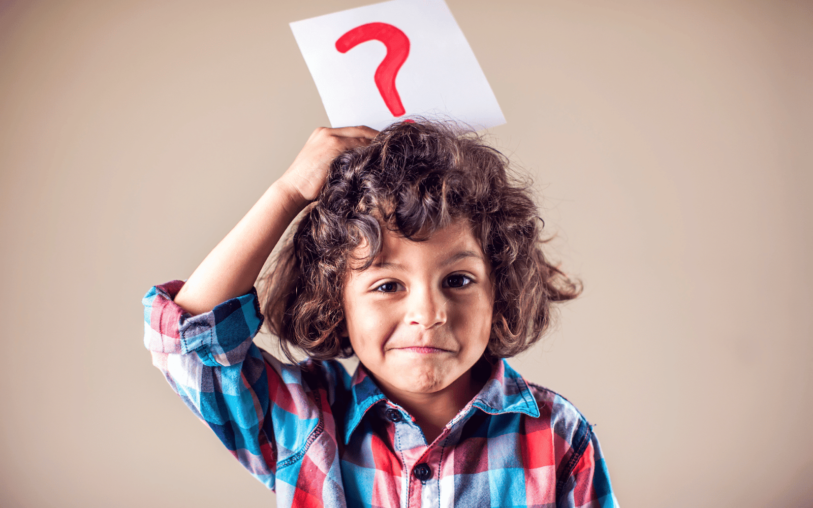 A child holding a piece of paper with a question mark on itDescription automatically generated