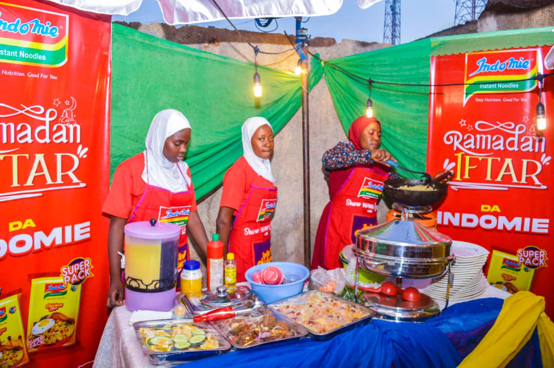 A group of women wearing red aprons standing in front of a table with food

Description automatically generated