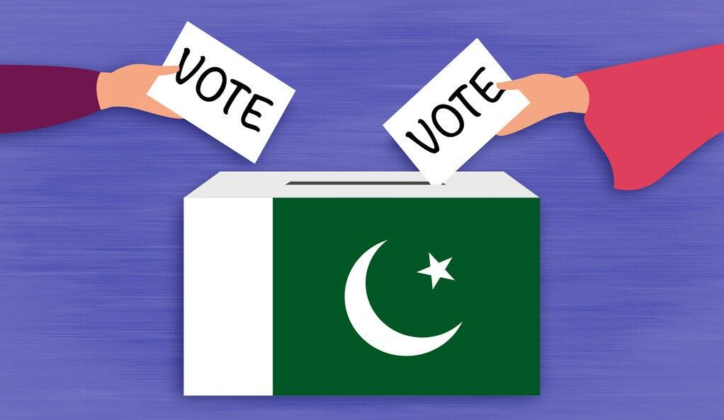 Two people dropping ballots into a box decorated with the Pakistani flag