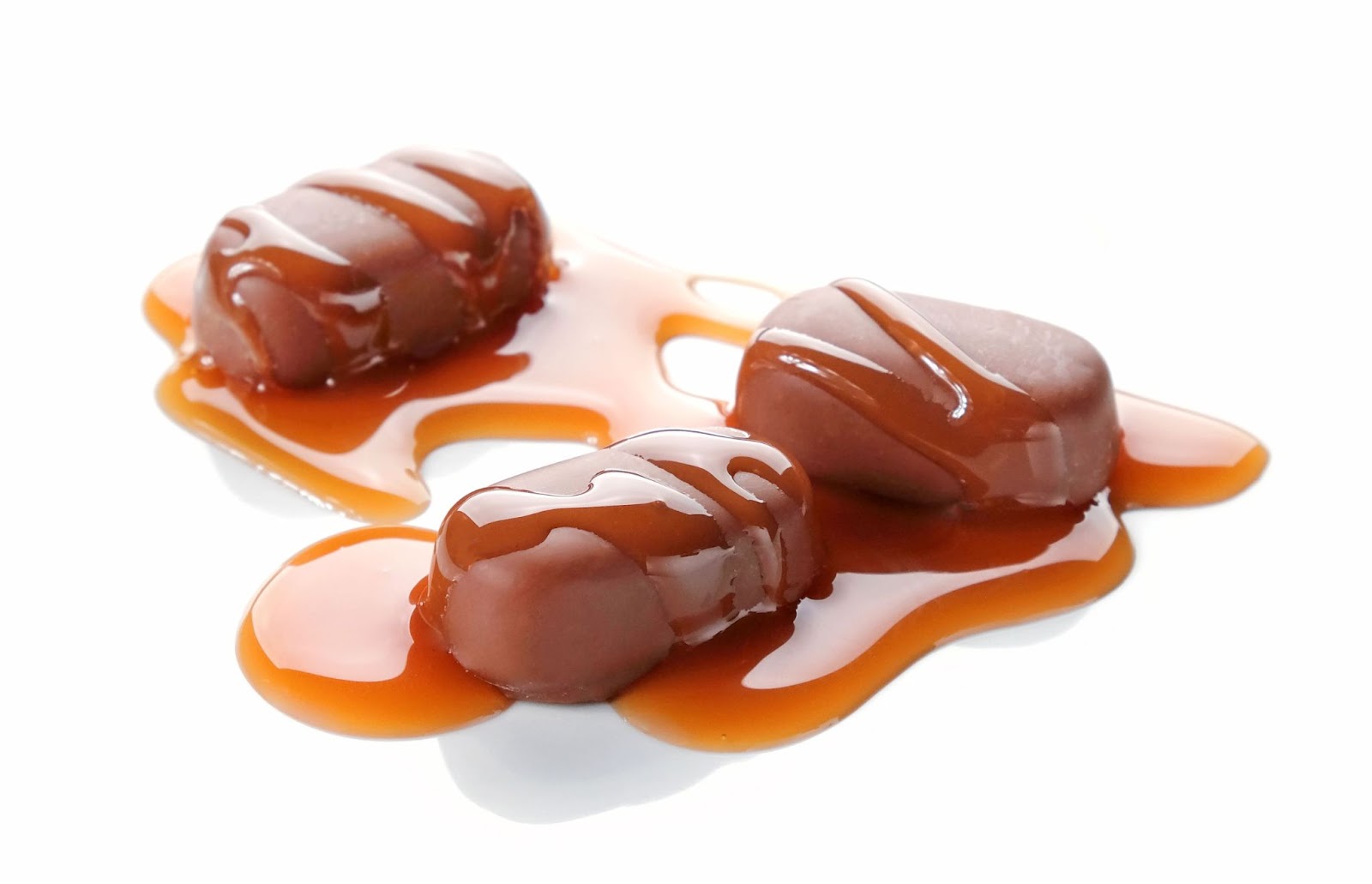 Three chocolate-covered caramel candies drizzled with rich caramel sauce, arranged appealingly on a simple background.
