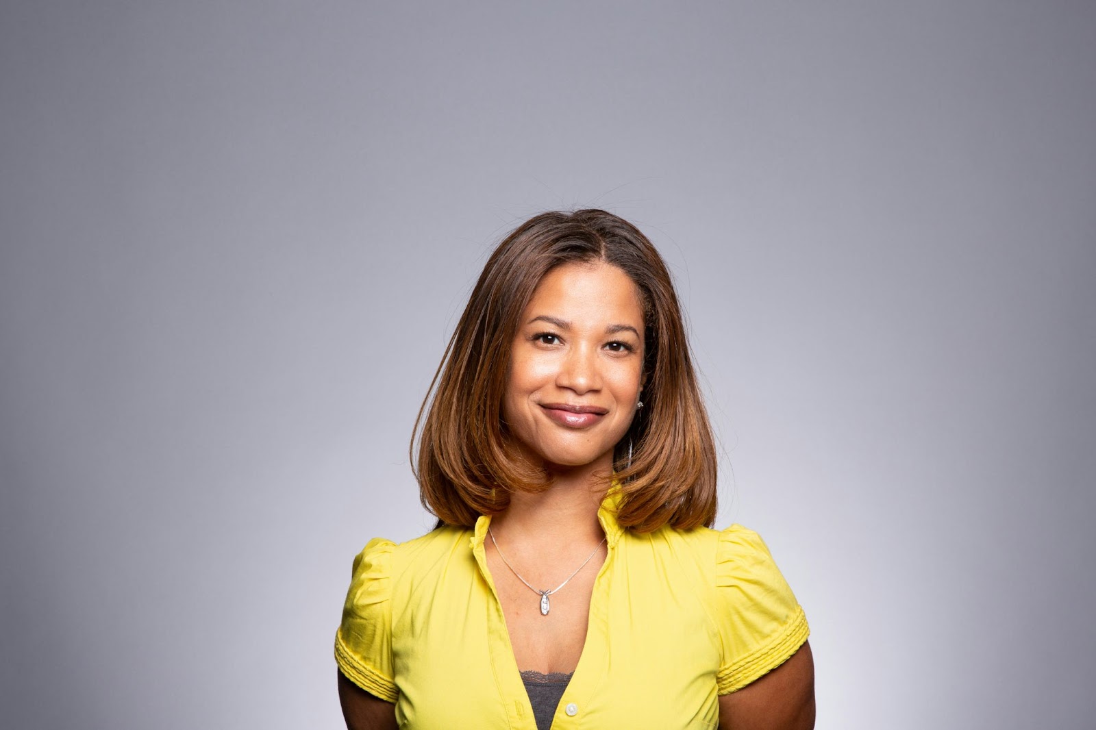 A woman dressed in simple attire is posing for her professional headshots with a smile on her face. 