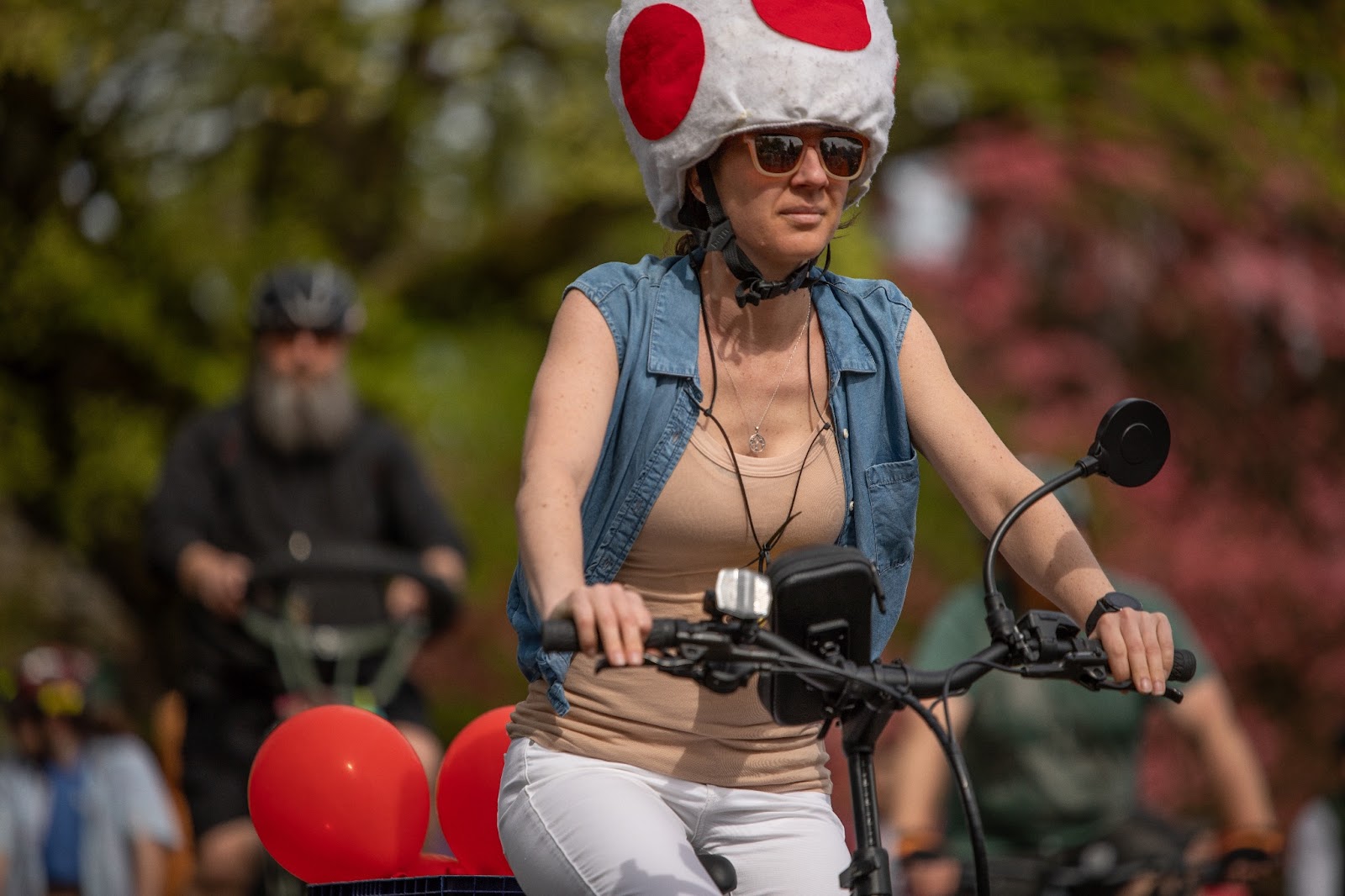 A woman on a bike who is not so much dressed as Toad from Mario Kart as she is just wearing the same kind of hat, at the Ladd's 500 relay in Portland in April of 2024.