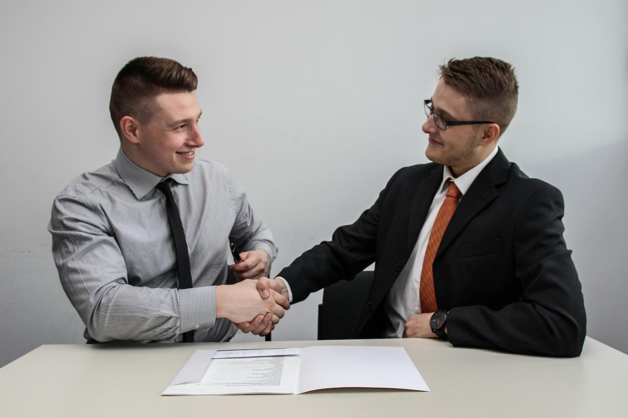 A man shaking hands with a team building speaker after they made a deal and signed a contract which is on a table in front of them.