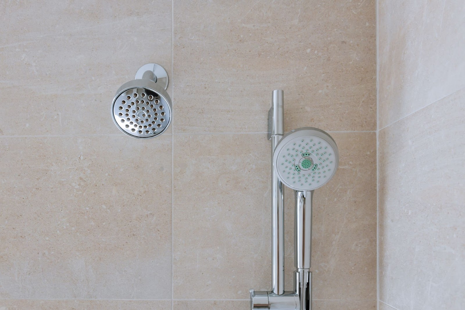 Two shower heads with tile in the background. 