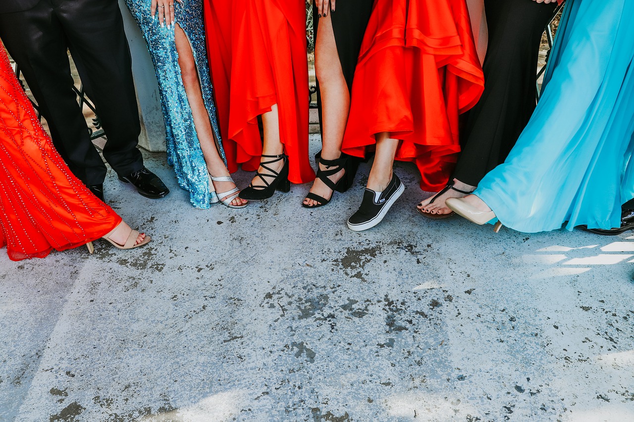 A group of individuals dressed formally, posing with one foot forward, in an image capturing their lower bodies. The occasion appears to be celebratory, resembling a prom or homecoming event.