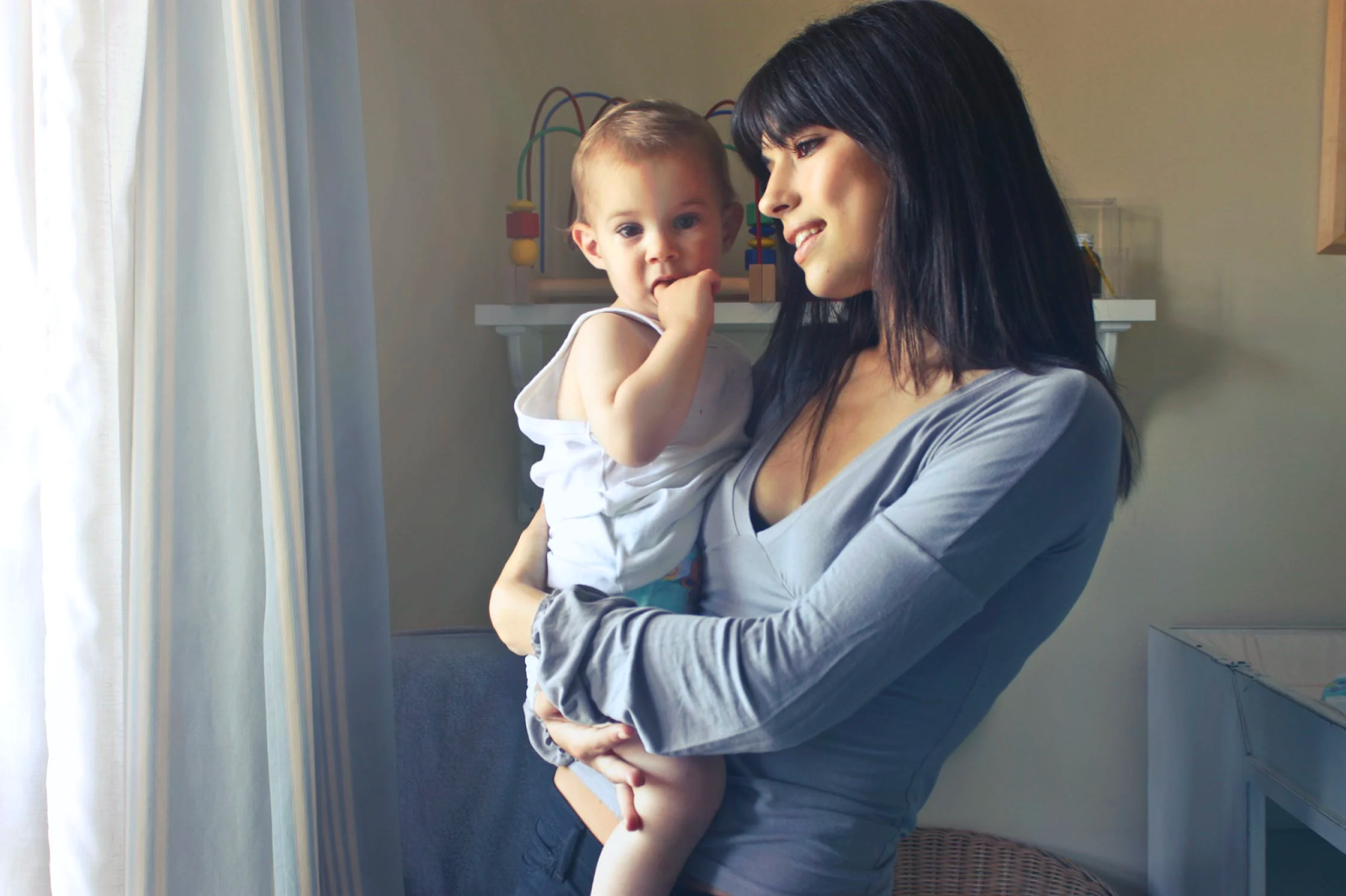 Young mother with black hair holding her baby by the window