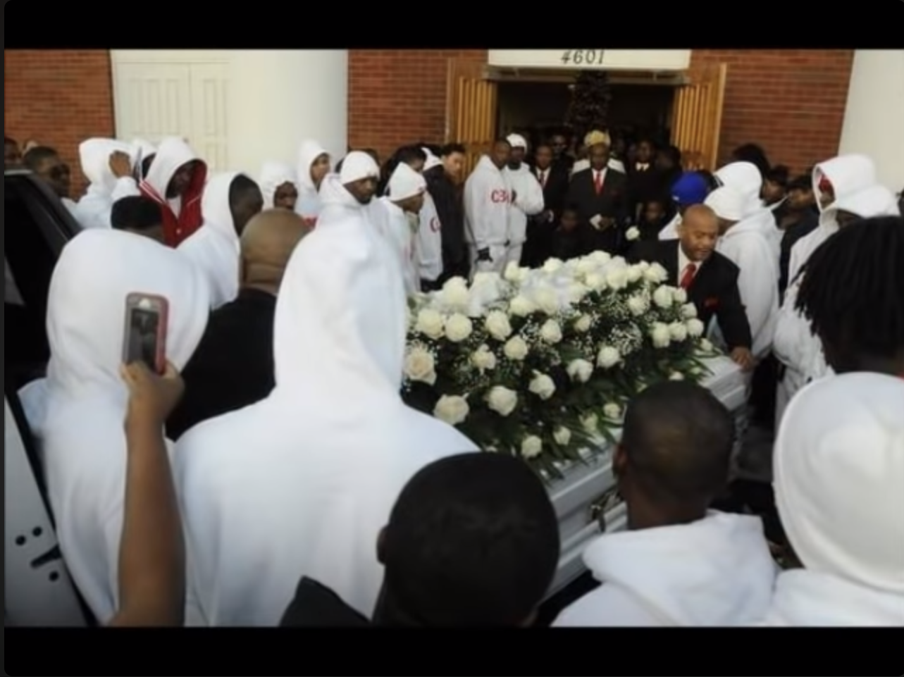 A group of people in white robes carrying a coffin

Description automatically generated