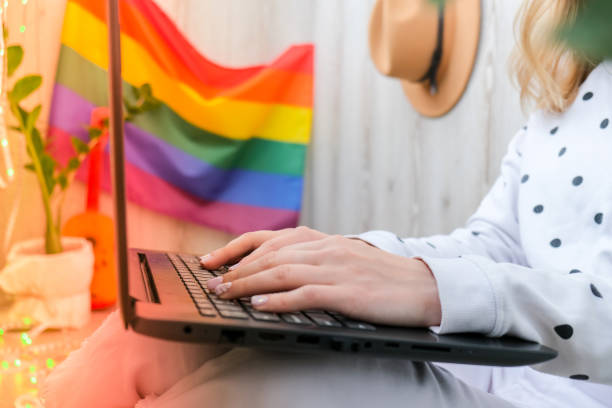 A woman working from home on a laptop with an LGBTQ+ flag in the background. 