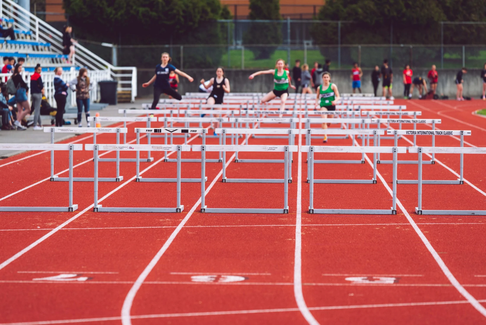 Athletes jumping over hurdles on track and field.