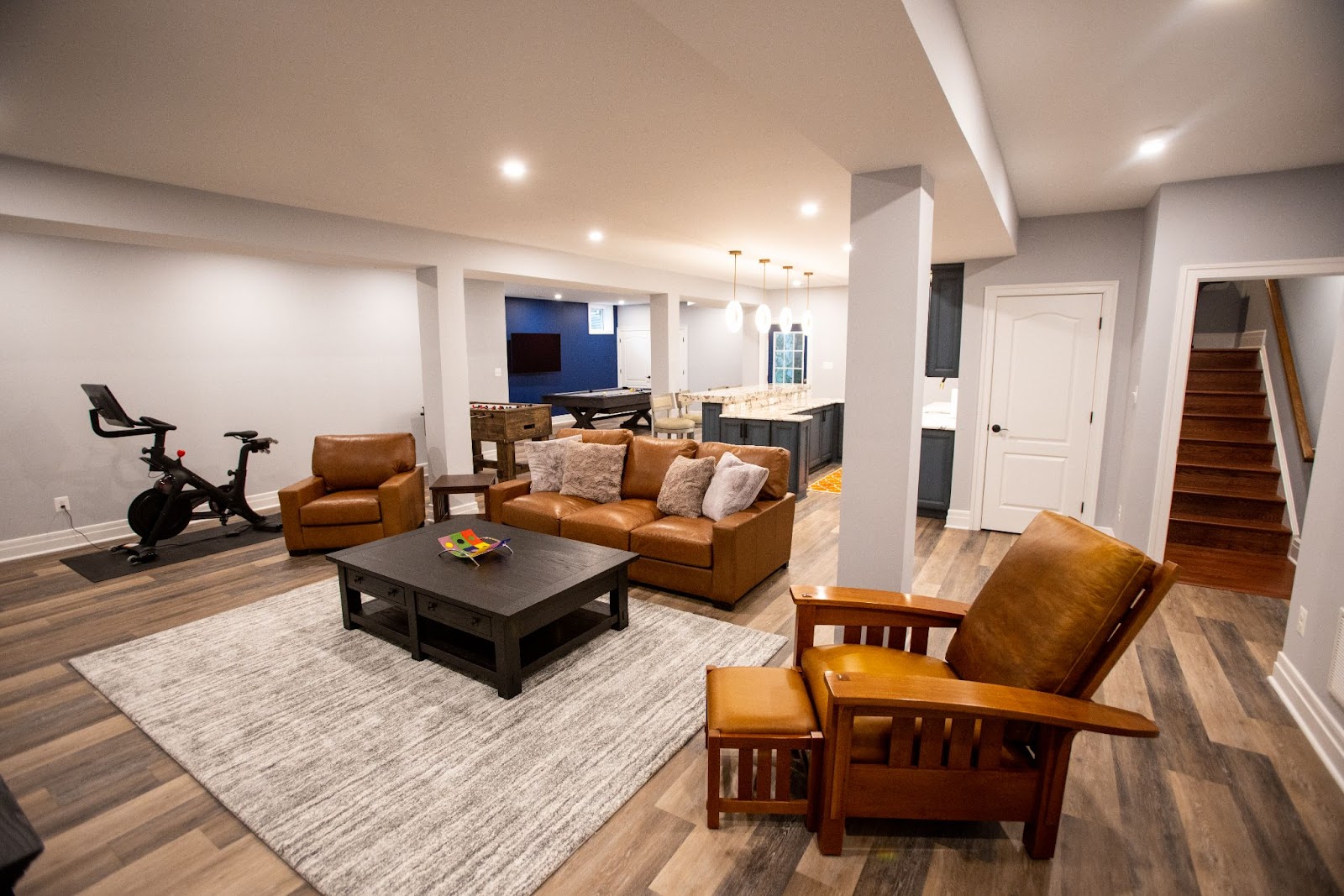 A spacious modern basement remodel in Herndon VA with grey flooring, leather sofas, a television, and an exercise bike.
