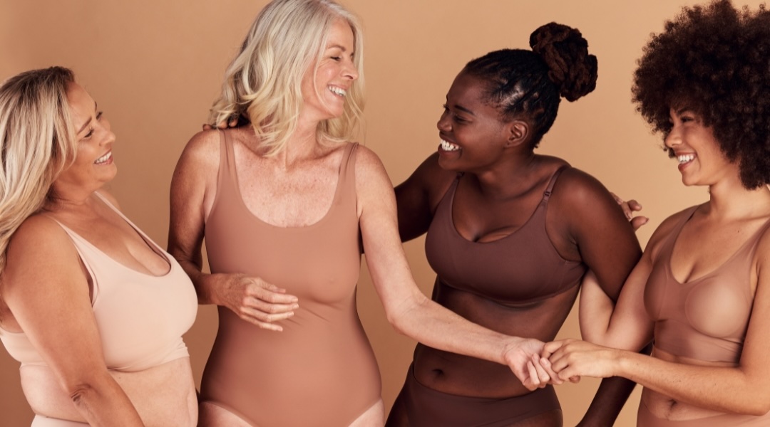 four smiling women with different body types and skin colors
