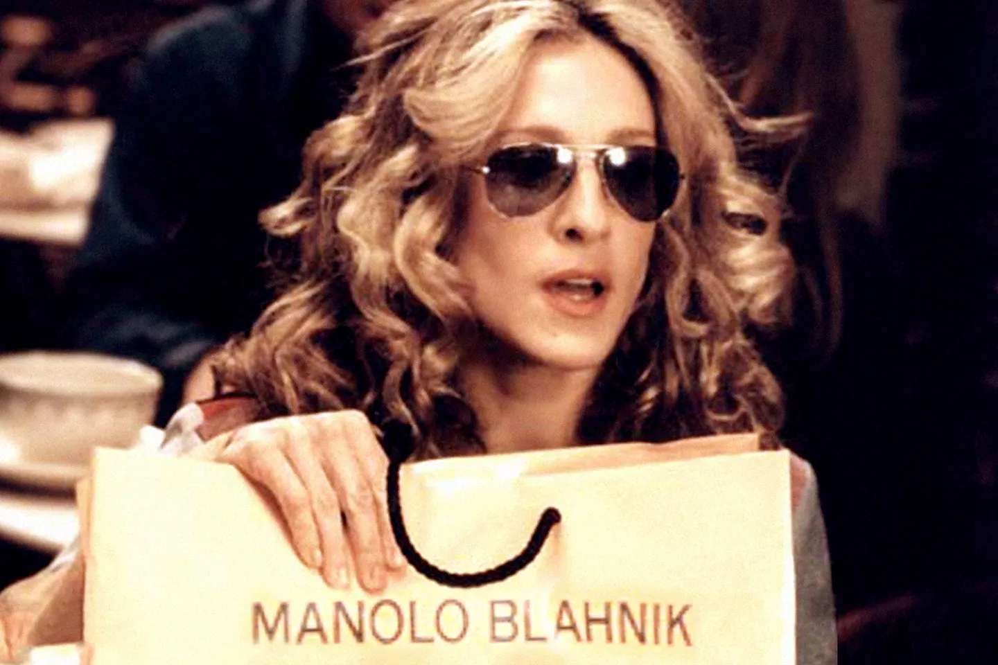Imagem da série "Sex and The City": Carrie Bradshaw mostrando sua compra, segurando a sacola Manolo Blahnik.