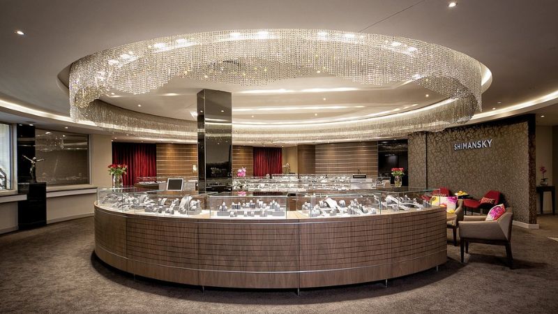Shimansky showroom in Cape Town, featuring a stylish and luxurious interior with a curved jewelry display counter under a glittering chandelier.

