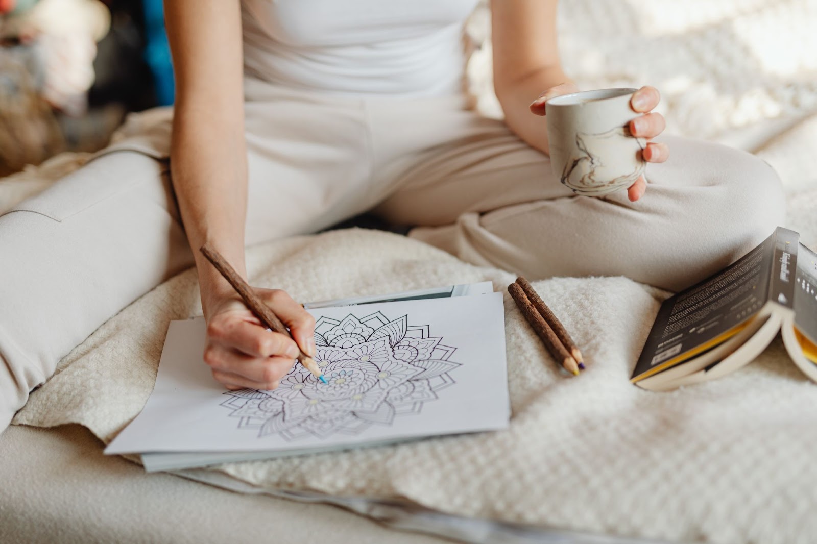 An adult using a coloring utensil to fill in a shape on a sheet, holding a mug in her left hand while enjoying a relaxing coloring activity.