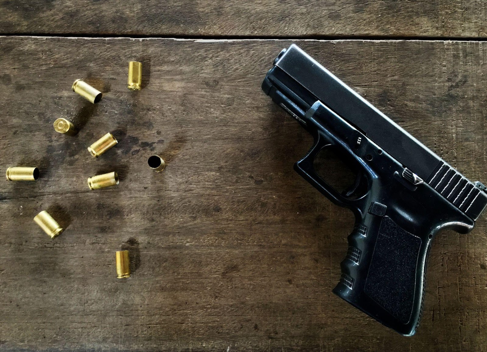 černá pistole a devět prázdných nábojnic na dřevěném stole