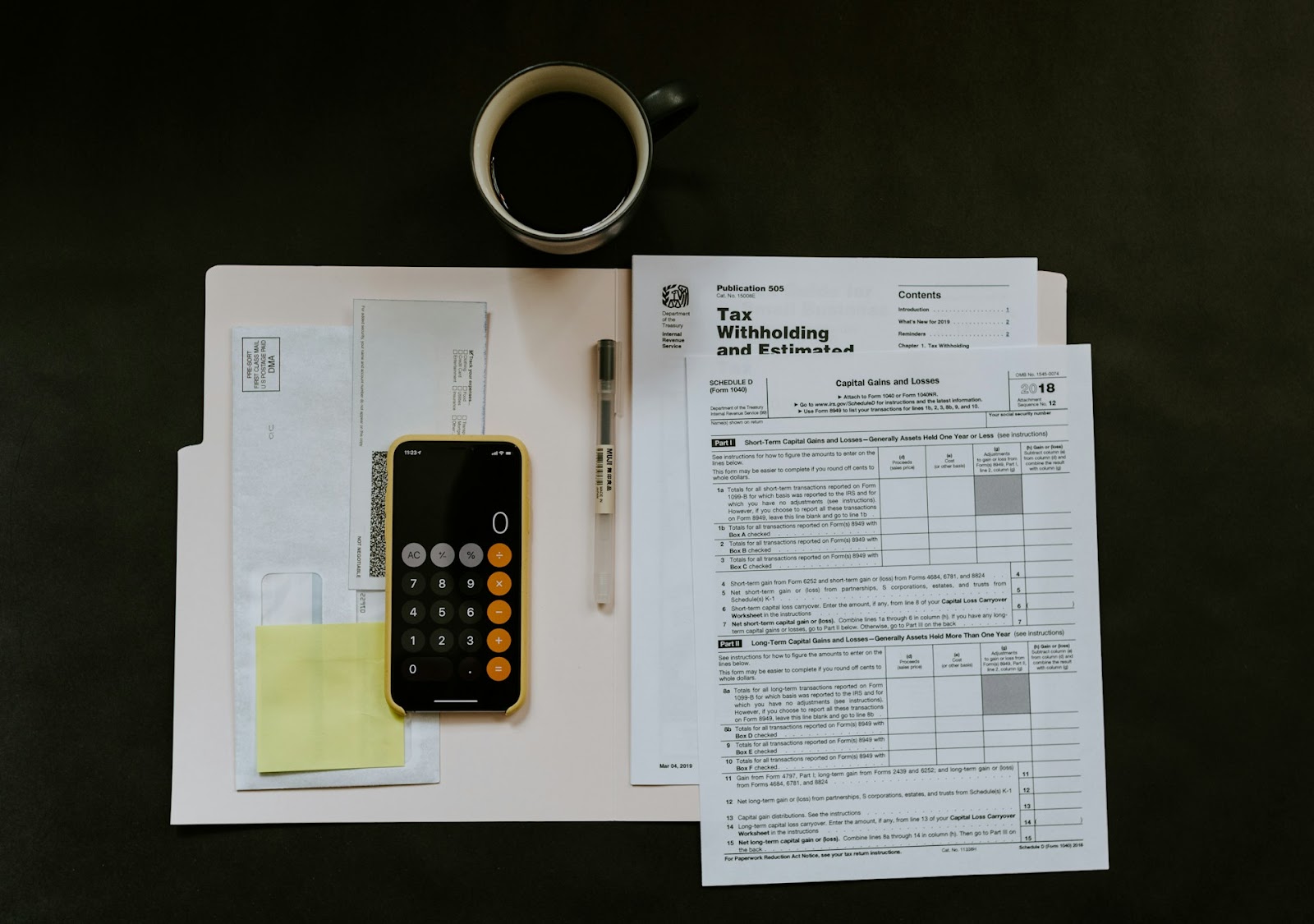 A flat lay of tax documents, envelopes, a calculator, a pen, sticky notes, and a cup of coffee