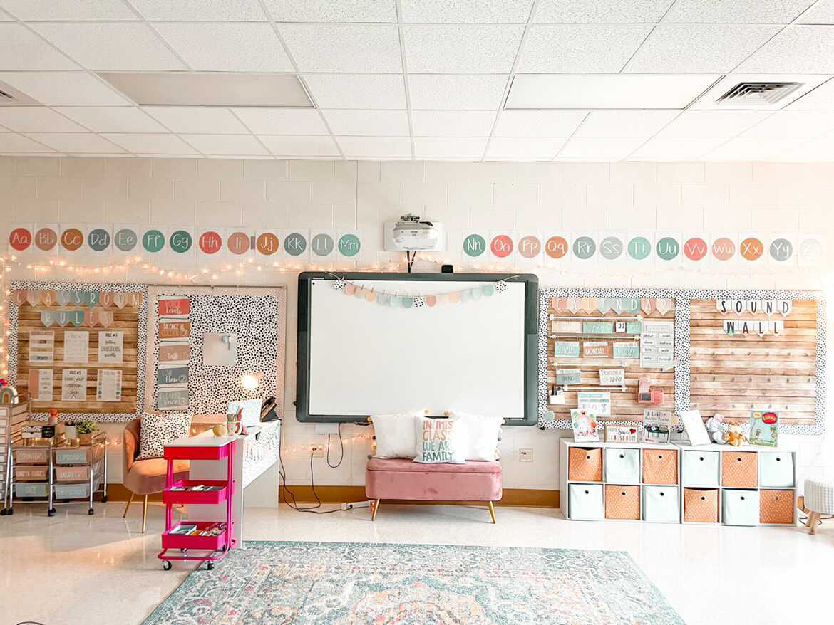 This image shows a the front of a classroom with twinkle lights up at the front of the bulletin boards, a giant rug on the floor, and other cozy elements. 