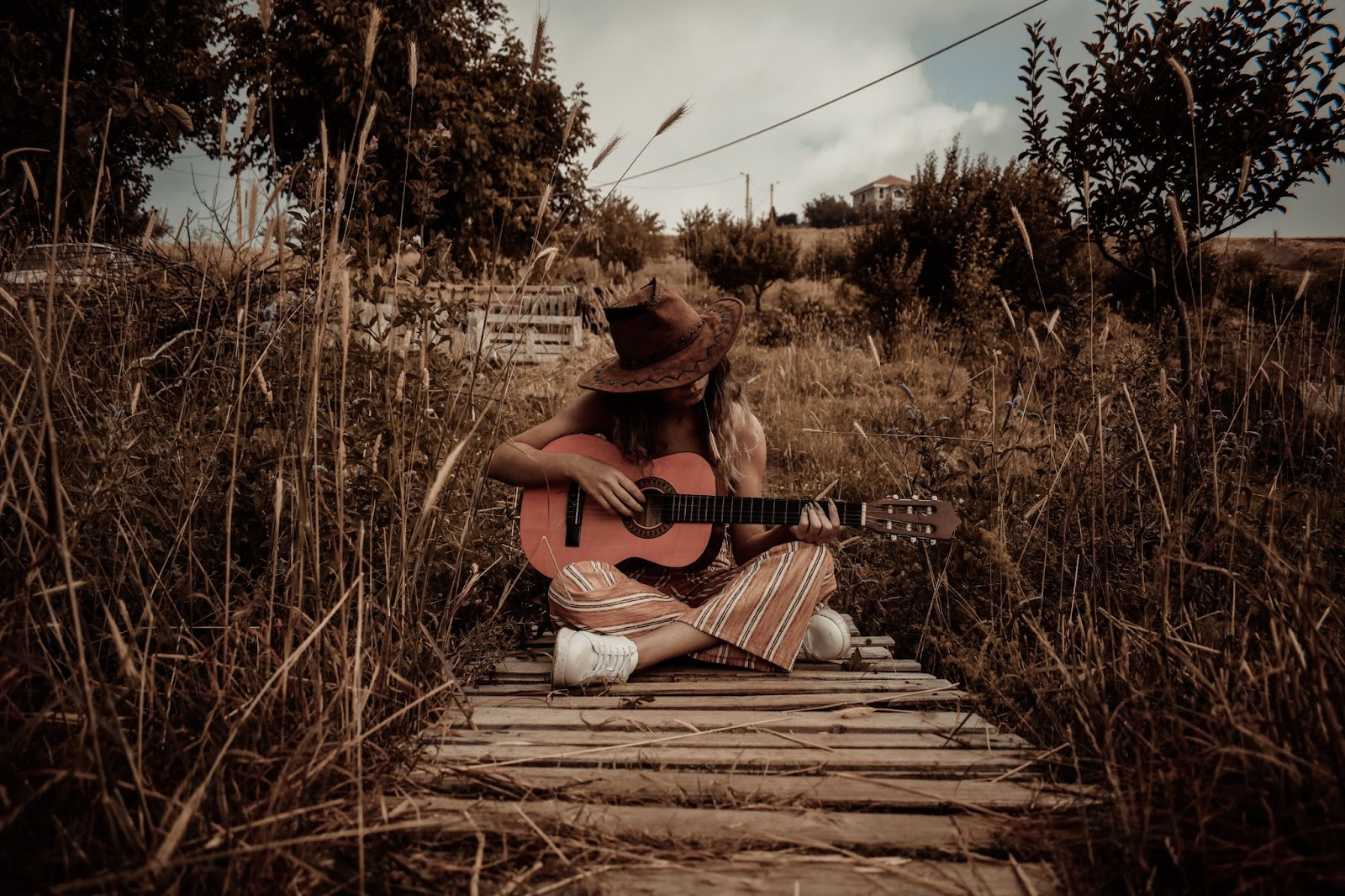 image of woman sitting and playing guitar on wooden path 