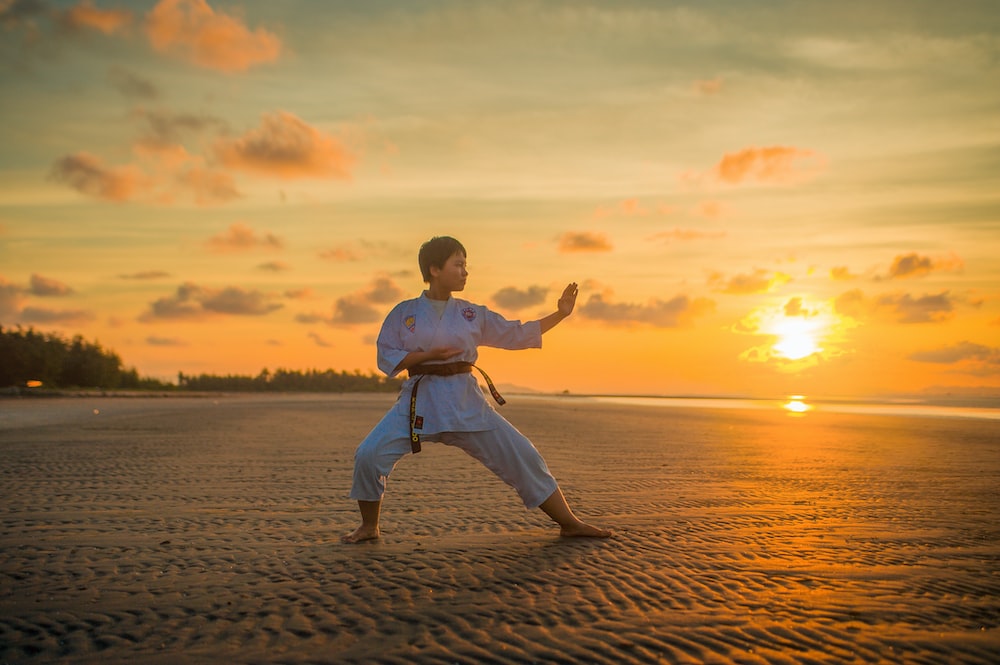 Person on a beach practicing martial arts. Sun is setting in the background.